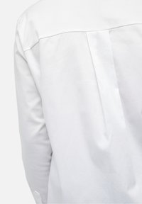 Camisa de algodón blanca con un detalle de yugo en la parte posterior, textura suave y un diseño simple y limpio con mínimas aberturas visibles.