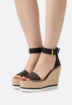 Wedge sandals with a black suede upper, ankle strap, and golden buckle detail. Features a woven jute platform and white rubber sole.