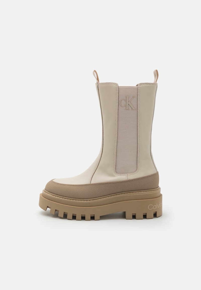 Botte Calvin Klein beige mi-mollet avec semelle à crampons épaisse, panneau latéral élastique, languettes de tirage et logo "cK" embossé sur la tige.