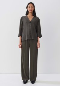 Haut en lin mélangé vert olive avec un décolleté en V, des manches trois-quarts et des détails de bouton blancs, associé à un pantalon large assorti.