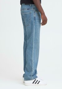Ljusblå denimjeans med rak passform, fem fickor och subtila sömdetaljer, bärs med vita sneakers.