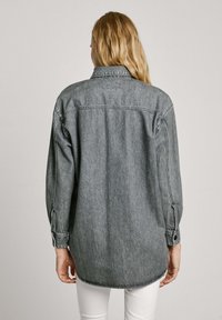 Lichtgrijze denimshirt met een kraag, lange mouwen en een afgeronde zoom. Opvallend door de zachte textuur en knoopdetails.