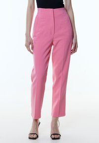 Hoge taille roze broek met een getailleerde pasvorm, voorzien van verticale naden, zijzakken en een zachte stoftextuur. Geaccentueerd met een strakke silhouet.