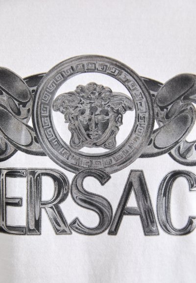 Valge kangas, millel on must ja hall graafiline disain, esitledes medaali näoga ja dekoratiivsete ahelate elementidega, ning tekst "VERSACE."