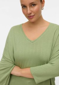 Haut vert clair à col en V avec texture côtelée verticale et manches trois-quarts. Présente une coupe décontractée et un tissu doux.