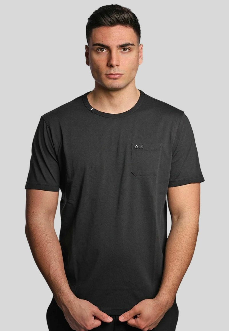 T-shirt nera a maniche corte in cotone, con taschino sul lato sinistro del petto e un piccolo logo, collo rotondo e vestibilità morbida.