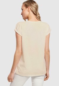 Beige T-Shirt mit kurzen Ärmeln und umgeschlagenen Ärmel, rundem Ausschnitt und lässiger Passform, aus weichem Baumwollstoff gefertigt. Minimalistisches Design.