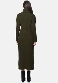 Olivgrünes, geripptes Strickkleid mit hohem Rollkragen, langen Ärmeln und figurbetonter Silhouette, die bis zur Mitte der Waden reicht, kombiniert mit schwarzen Stiefeletten.