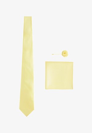 Yellow silk tie, matching pocket square, and flower lapel pin arranged on a white background.