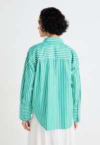 Grønn og hvit stripete skjorte med en litt oversized passform, knappede mansjetter og klassisk krage; stoffet ser glatt og lett ut.