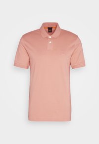 Polo en coton rose pâle, doté d'un col à boutons, de manches courtes et d'un discret patch logo sur la poitrine. Texture lisse.