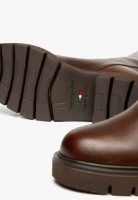 Braune Lederstiefel mit glatter Oberfläche und runder Zehenform. Dicke braune Gummisohle mit tiefem Profil und geprägtem Markenlogo.