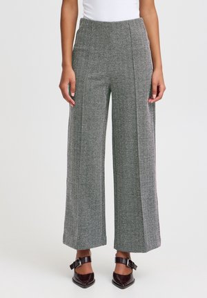 Woman wearing high-waist wide-leg gray herringbone pants paired with white top and dark brown pointed shoes with buckles.