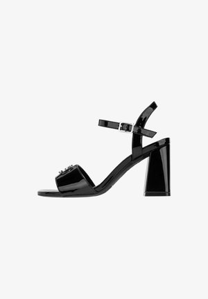 Schwarze Lackleder-Blockabsatzsandalen mit einem breiten Riemen über den Zehen, verstellbarem Knöchelriemen, Blockabsatz und dekorativen Verzierungen.