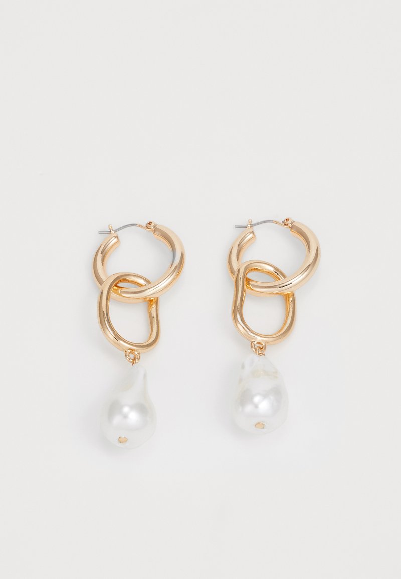 Gullfargede øreringer med sammenvevde løkker som har en blank finish, og en hvit, tårnformet perle hengende fra bunnen.