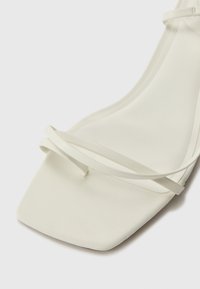 Hvite stroppesandaler med firkantet tådesign, glatt tekstur, tynne stropper og minimalistisk konstruksjon. Egnet for formelle anledninger.
