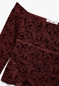 Burgundowy top z długim rękawem, z kwiatowym wzorem z aksamitu, z dekoltem odsłaniającym ramiona i warstwowym wykończeniem dolnej części. Metka głosi "olé by ketton."