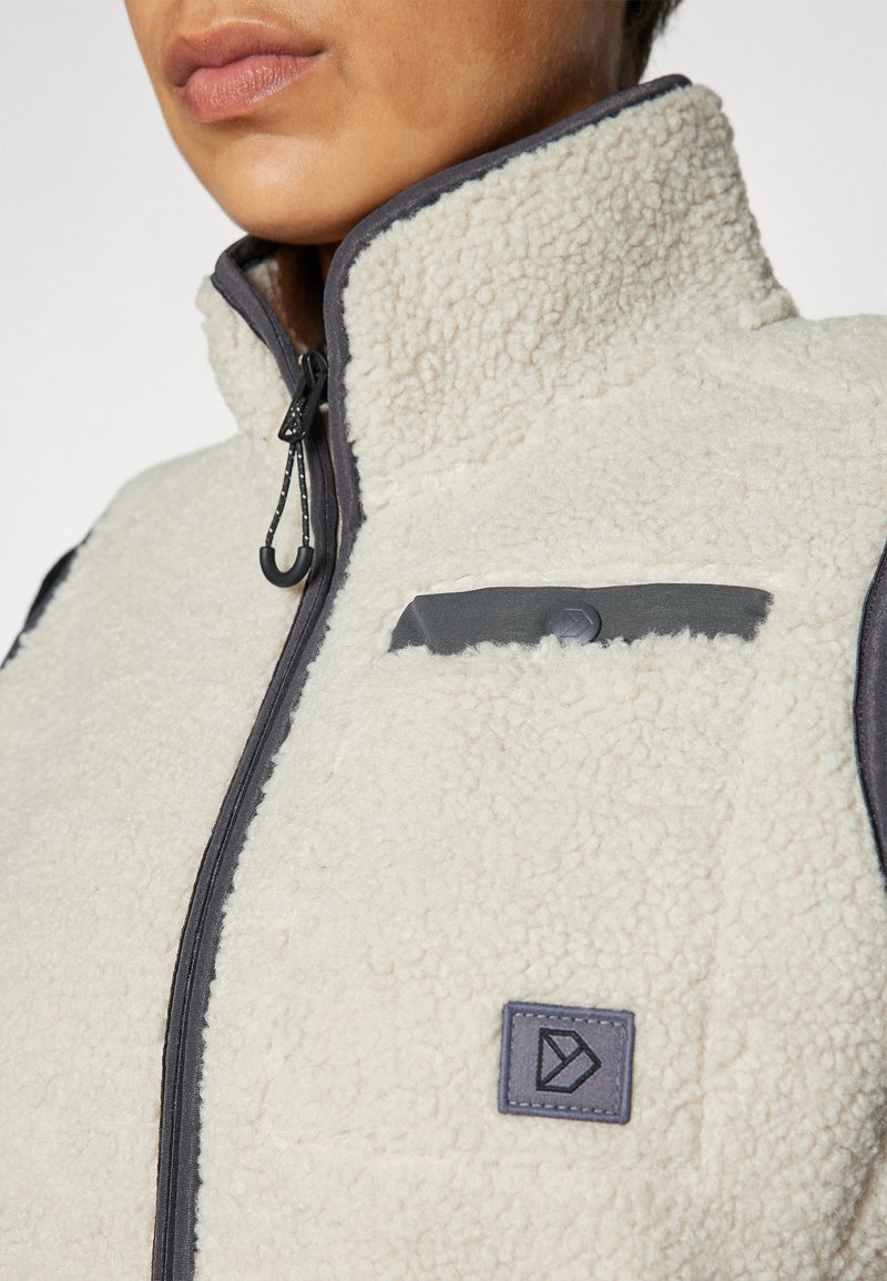 Fleecejacke mit hohem Kragen, in Cremefarbe, mit Reißverschluss und schwarzen Akzenten. Sie verfügt über eine aufgesetzte Tasche und ein Branding-Detail.