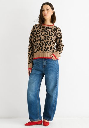 Tansweater mit Leopardenmuster und roten gerippten Abschlüssen, kombiniert mit blauen weiten Jeans und roten Ballerinas. Die Textur erscheint weich und gemütlich.