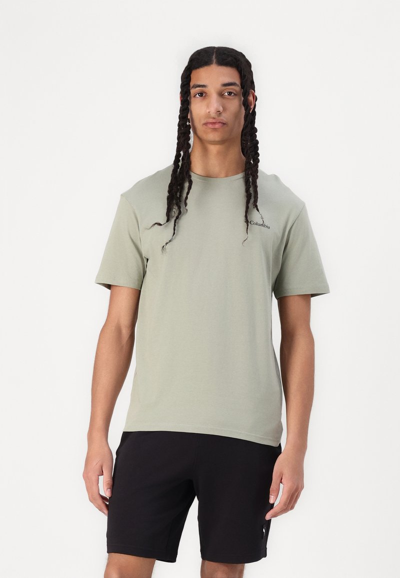 Camiseta de algodón verde claro con mangas cortas, cuello redondo y un logo sutil en el pecho; combinada con pantalones cortos negros. Textura suave.