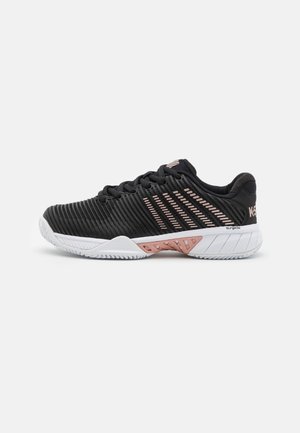 Chaussures de sport noires avec une tige texturée, soulignée de rayures rose pâle. Elles présentent une semelle blanche avec un motif géométrique et un talon renforcé.