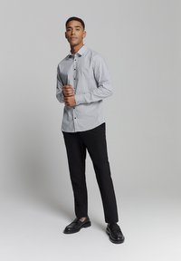 Overhemd met knopen en een geometrisch patroon in zwart en wit, met lange mouwen, gecombineerd met zwarte rechtlopende broeken en zwarte schoenen.