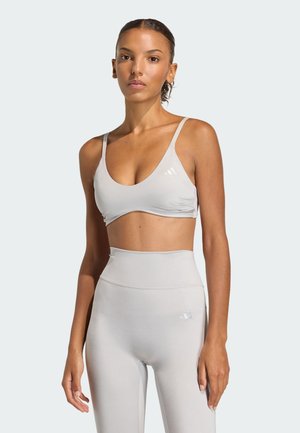 Light gray sports bra and high-waisted leggings in smooth fabric. Features thin straps and minimal branding. Simple, modern design.