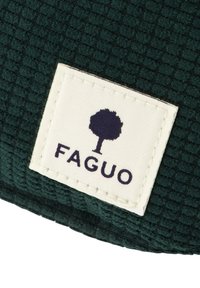 Tessuto verde texturizzato con motivo a griglia; etichetta bianca con logo ad albero e "FAGUO" in carattere blu scuro.