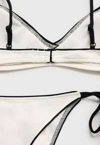 White bikini top with black trim, featuring adjustable straps and a textured design. Bottom piece with side ties and matching color scheme.