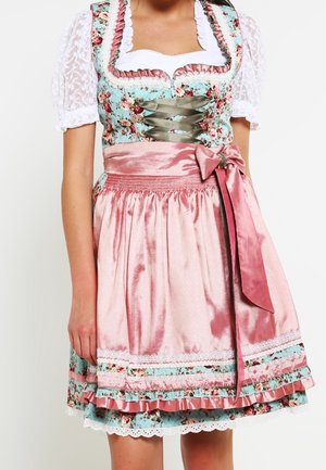 Femme portant une robe traditionnelle dirndl fleurie avec des manches en dentelle blanche et un tablier rose brillant noué en nœud sur le côté.