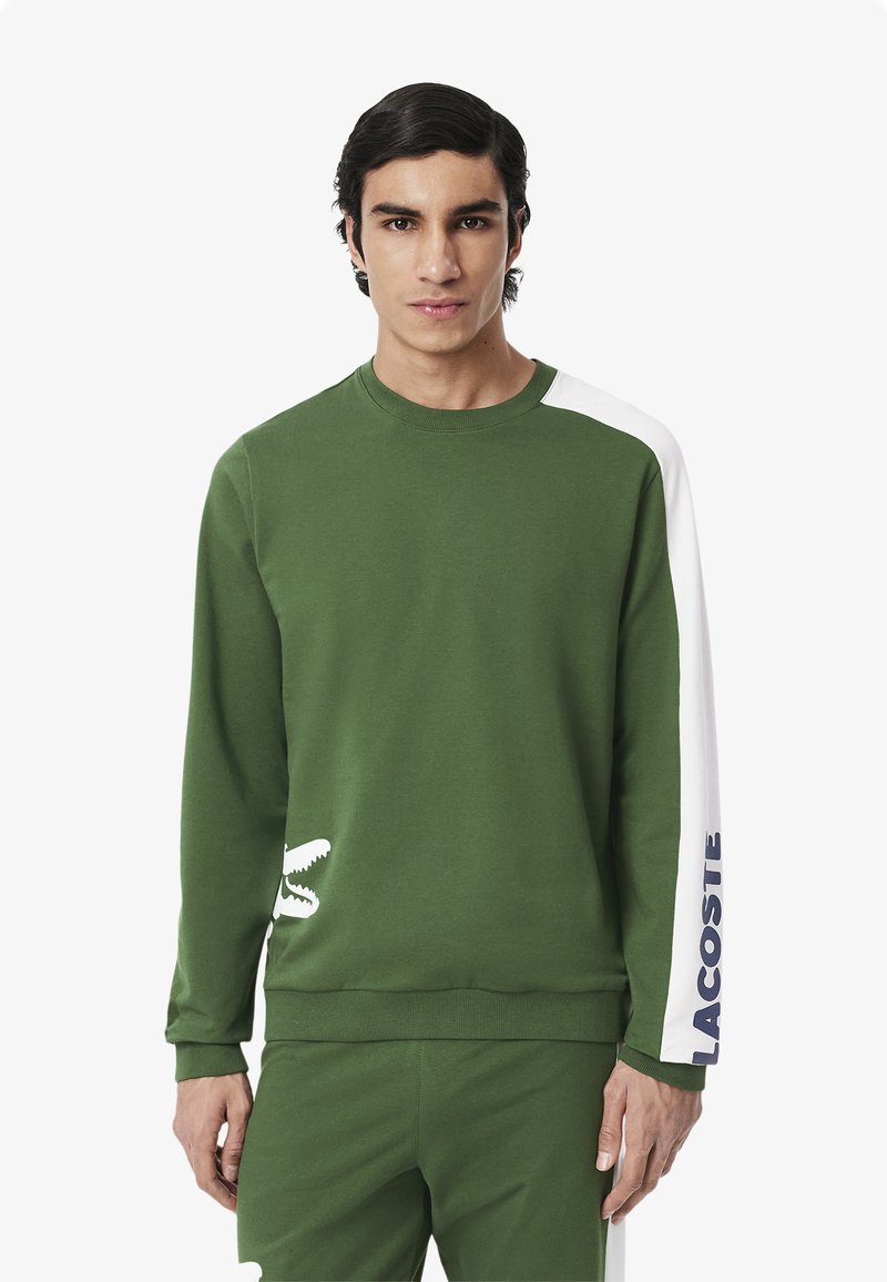 Felpa verde con collo a girocollo, caratterizzata da dettagli bianchi sulle spalle e il testo 'Lacoste'. Tessuto morbido con dettaglio del logo coccodrillo.