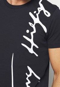 T-shirt in cotone nero con una grande grafica astratta bianca sul lato sinistro. Collo rotondo classico e maniche corte.
