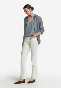 Ljusblå genomskinlig skjorta med knappar över en grå linne, matchat med vita raka byxor och bruna platta skor. Släta texturer och avslappnad passform.