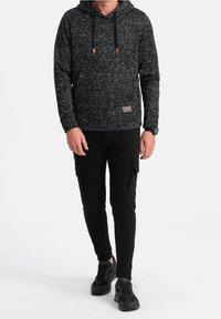 Černá a šedá melírovaná mikina s kapucí na stažení, s texturovanou látkou a malou logo nášivkou, kombinovaná s černými pracovními kalhotami a teniskami.