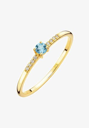 Gouden ring met een centrale ronde lichtblauwe edelsteen, omgeven door kleine heldere stenen langs de band. Gladde, gepolijste afwerking.