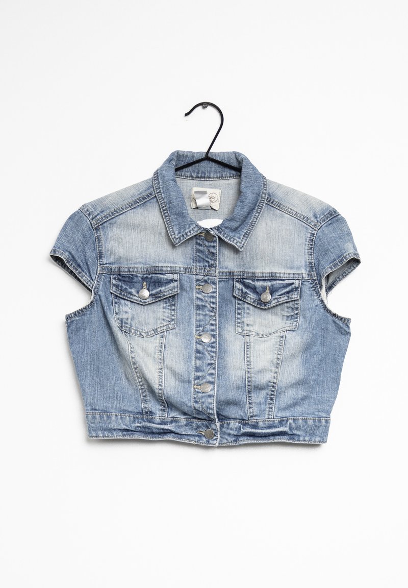 Veste en jean courte bleu clair avec manches courtes, boutons devant et deux poches poitrine boutonnées suspendue sur un cintre noir.