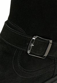 Czarne zamszowe buty za kostkę z szerokim paskiem i metalową srebrną klamrą oraz kontrastowym przeszyciem wzdłuż krawędzi dla dodatkowego akcentu.