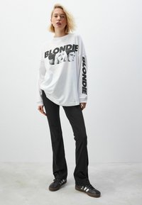 Wit sweatshirt met lange mouwen, voorzien van een zwarte grafische print van drie gezichten en de tekst "BLONDIE" op de borst en mouw. Te combineren met zwarte broek.