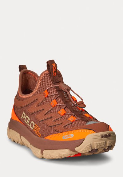 Brauner Sportschuh mit orangen Akzenten, strukturiertem Mesh-Obermaterial, Gummisohle und Schnürsenkeln; verfügt über ein Logo an der Seite und eine Schlaufe am hinteren Teil.