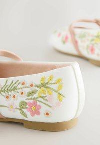 White ballet flats featuring floral embroidery in pink, yellow, and green. The shoes have a soft texture and a light pink strap.
