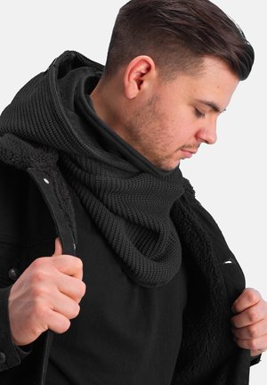 Black knitted scarf with a textured pattern, worn around the neck; layered under a black jacket with a soft fleece lining.