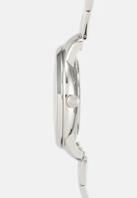 Montre-bracelet en métal argenté avec un boîtier rond lisse, une couronne texturée et un design de bracelet à maillons. La surface a une finition polie.