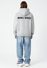 Felpa grigia con la scritta "MIRA PARIS" stampata in nero sulla schiena, abbinata a jeans in denim azzurro chiaro, larghi, e sneakers bianche.