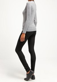 Camisa gris de manga larga combinada con pantalones negros ajustados y zapatos negros de cordones. La tela parece suave con un diseño ceñido.