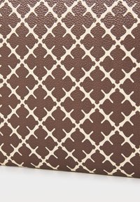 Brunt strukturert materiale med et gjentakende kremfarget geometrisk mønster, med diamant- og korsformer gjennom overflaten.