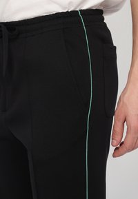 Black joggers with a smooth texture feature a contrasting light green side stripe and an elastic waistband with drawstring and side pocket.