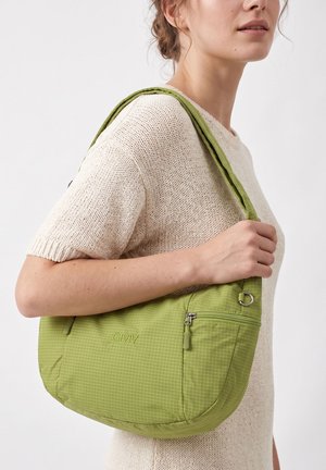 Persona che indossa un maglione lavorato a maglia crema e tiene una borsa a tracolla verde con tasca con cerniera e motivo a griglia sottile.