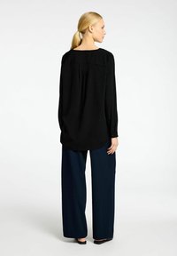 Sort langærmet bluse med rund hals, der har en bagpigl. Sættet inkluderer løse, mørkeblå brede bukser og flade sorte sko.