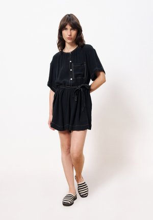 Zwart korte mouwen jurk met zak, knoopdetail en ceintuur op taille. Gecombineerd met gestreepte instappers. Glad stoffen textuur.