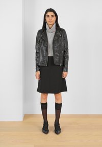 Veste en cuir noir, pull à col roulé gris, jupe noire, chaussettes en voile noires, chaussures à bout pointu noires. Design simple, silhouette ajustée et superpositions.
